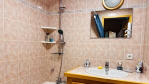 A bathroom with a bathtub, a sink, and a mirror. There is a showerhead above the bathtub and a shelf with toiletries. - Cozy T2 Apartment with Terrace, 5 pers, Les Saisies (Les Saisies)