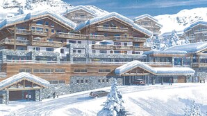 Et snedækket lodge med flere træhytter og balkoner, foran et bjerglandskab.