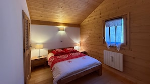 Et hyggeligt soveværelse med træloft, seng med rødt og hvidt sengetøj, to sengeborde med lamper og et vindue med gardin.