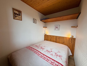 A bedroom with a wooden headboard, a bed with a white and red patterned bedspread, and two wall-mounted light fixtures.