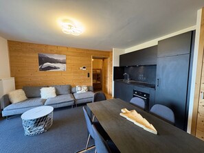 Un interior moderno con sofá, mesa de comedor, zona de cocina y una pared de madera con un cuadro.