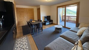Ein Wohnzimmer mit einer Couch, einem Fernseher, einem Esstisch mit Stühlen und einer Glastür zum Balkon.