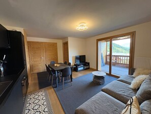Ein Wohnzimmer mit einer Couch, einem Fernseher, einem Esstisch mit Stühlen und einer Glastür zum Balkon.