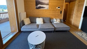Un intérieur moderne avec un canapé d’angle gris, une table basse ronde et un mur en bois orné d’un tableau encadré.