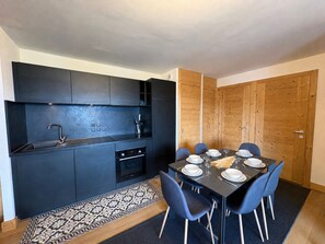 Eine kompakte Küche mit modernen Geräten, ein Essbereich mit Tisch für vier Personen und eine Holztür.