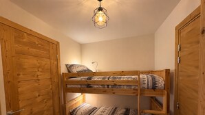 Ein Etagenbett mit gemusterten Betttextilien, eine Nachttischlampe und eine Pendelleuchte in einem Raum mit Holztüren und -wänden.