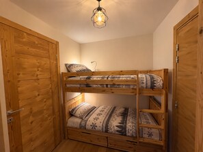 Ein Etagenbett mit gemusterten Betttextilien, eine Nachttischlampe und eine Pendelleuchte in einem Raum mit Holztüren und -wänden.