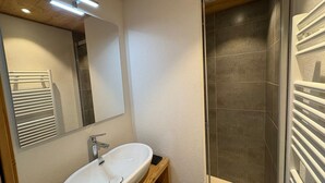 Ein Badezimmer mit weißem Waschbecken, einem Spiegel und einem Duschbereich mit dunklen Fliesen.