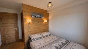Une chambre à coucher avec une tête de lit en bois, un lit recouvert d’une literie à motifs, deux lampes fixées au mur et un luminaire au plafond.