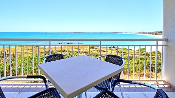 A balcony with a table and chairs, overlooking a beach with clear blue water and a distant shoreline. - Spacious Studio with View and Pool in Mont Vernon (Saint-Martin)