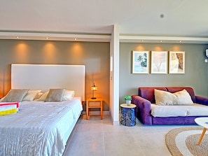 A modern bedroom with a large bed, bedside table with a lamp, a purple sofa, and three framed pictures on the wall. - Spacious Studio with View and Pool in Mont Vernon (Saint-Martin)