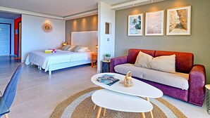 A modern living room with a sofa, a coffee table, and a bed with a headboard. There are framed pictures on the wall and a small table with a plant. - Spacious Studio with View and Pool in Mont Vernon (Saint-Martin)