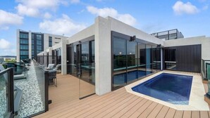 A modern rooftop with a swimming pool, glass railings, and a wooden deck. - Luxury Apartment in Canberra CBD (Reid)
