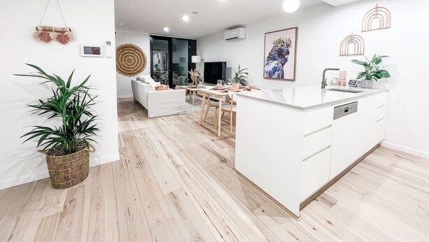 A modern kitchen with white cabinetry, a central island, and a dining area with a white sofa and wooden table. - Luxury Apartment in Canberra CBD (Reid)