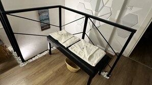 A corner room with a black metal staircase, a white wall with hexagonal patterns, and a wooden floor.