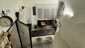A compact kitchen with a dining area, a clock, and a patterned rug.