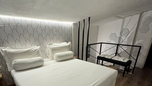 A modern bedroom with a large bed, a small bench, and a geometric wall design.