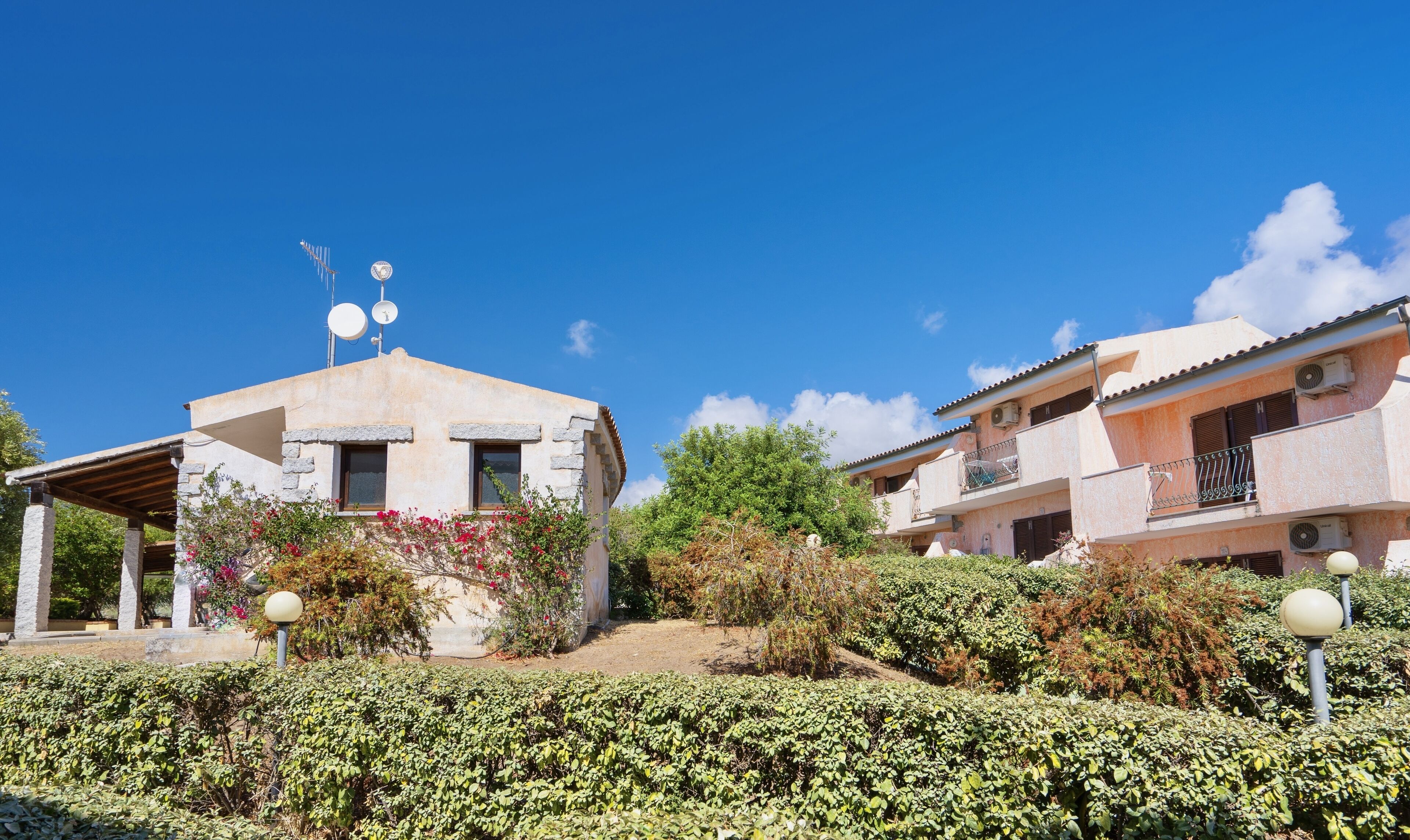 A building with a stone facade, satellite dishes, and a small garden with red flowers.
