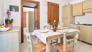 Un coin repas avec une table en bois, dressée pour quatre personnes, entourée de chaises assorties. Un saladier rempli de fruits et une plante en pot sont posés sur le comptoir.