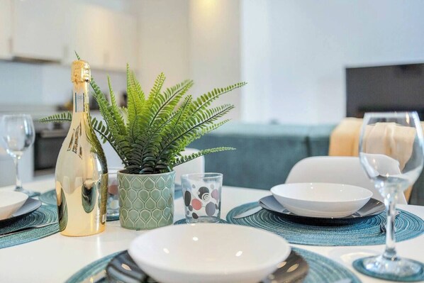 A dining table set with plates, glasses, a bottle, and a fern plant.