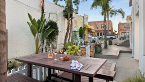 Un patio al aire libre con mesa de madera dispuesta para dos personas, con un plato de fruta y dos copas de vino.