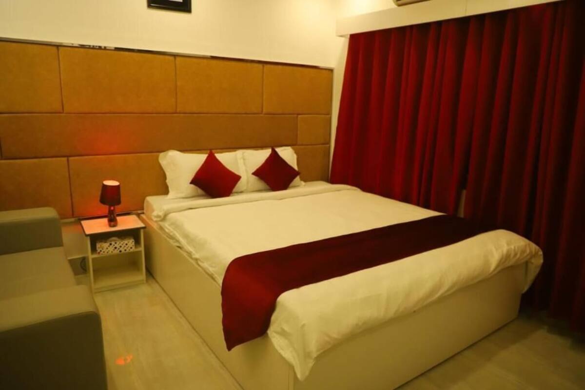 A hotel room with a large bed, a nightstand with a lamp, and a red curtain.