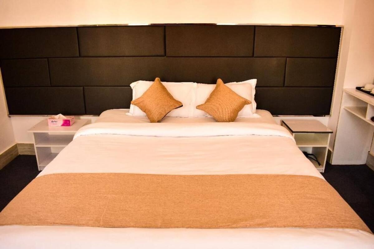 A neatly made bed with a dark headboard, two pillows, and a brown throw blanket.