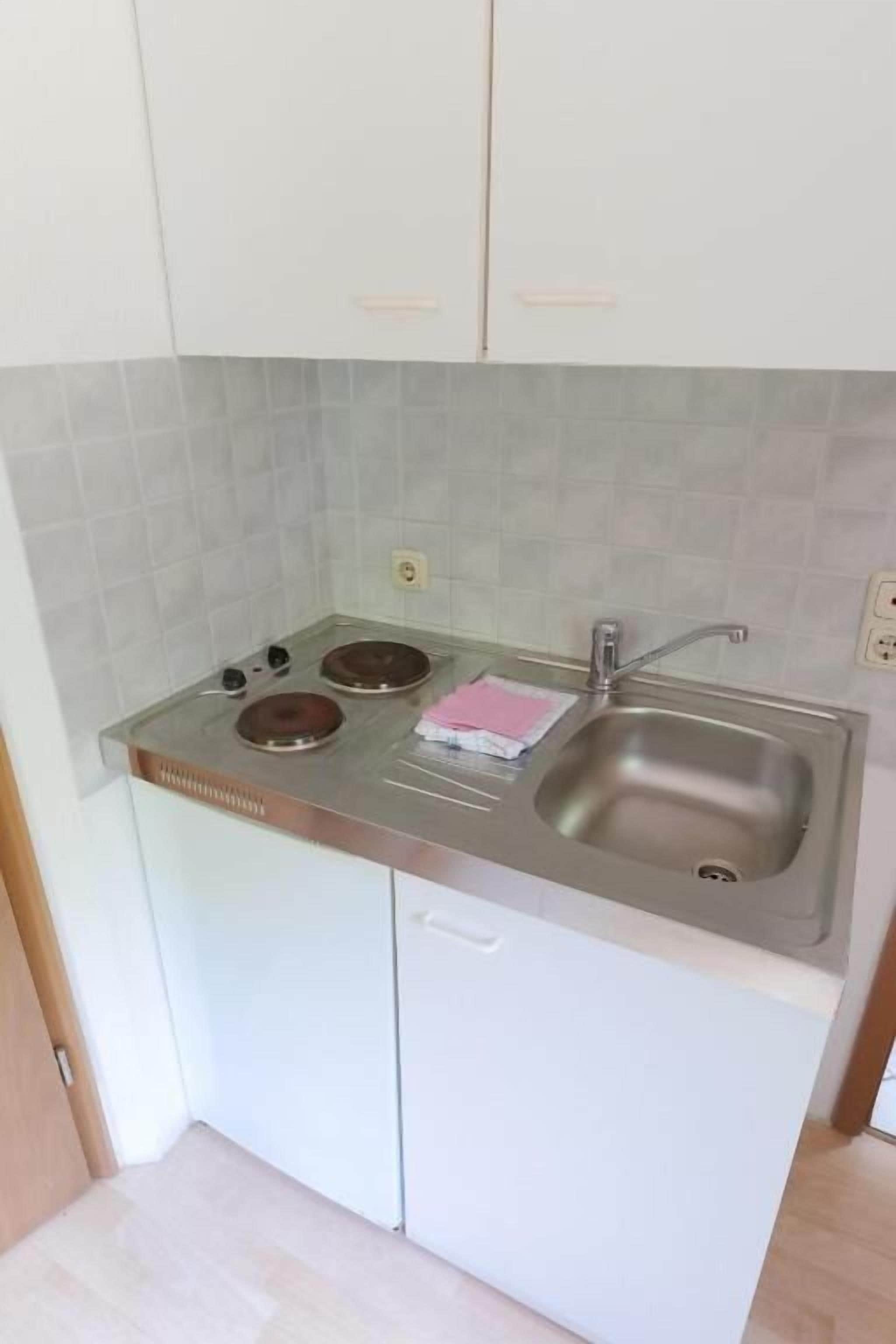 Une cuisine de taille réduite, avec des meubles blancs, un évier en acier inoxydable et une cuisinière à gaz.