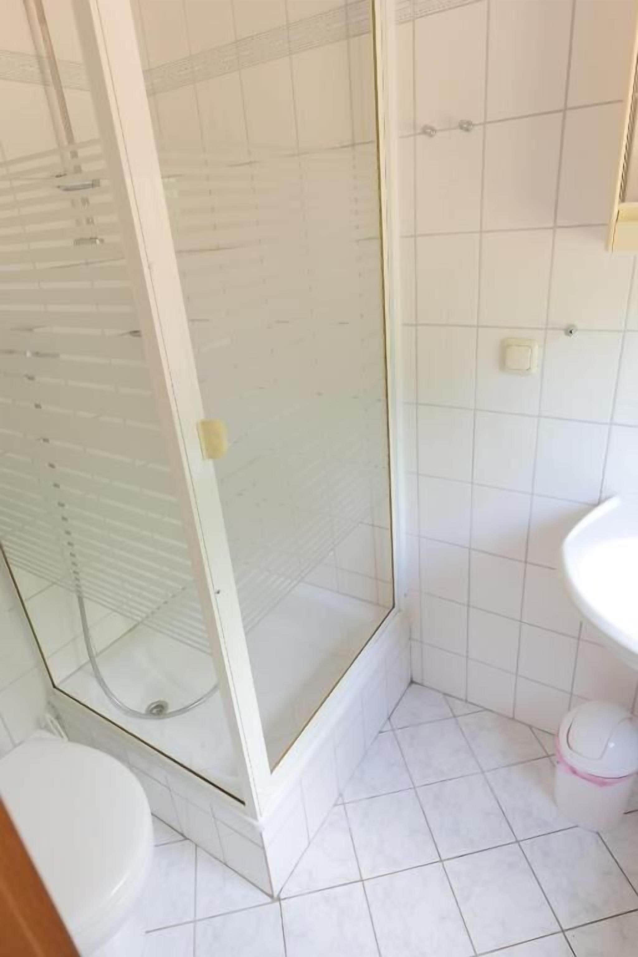 A bathroom with a glass shower enclosure, a toilet, and a sink.