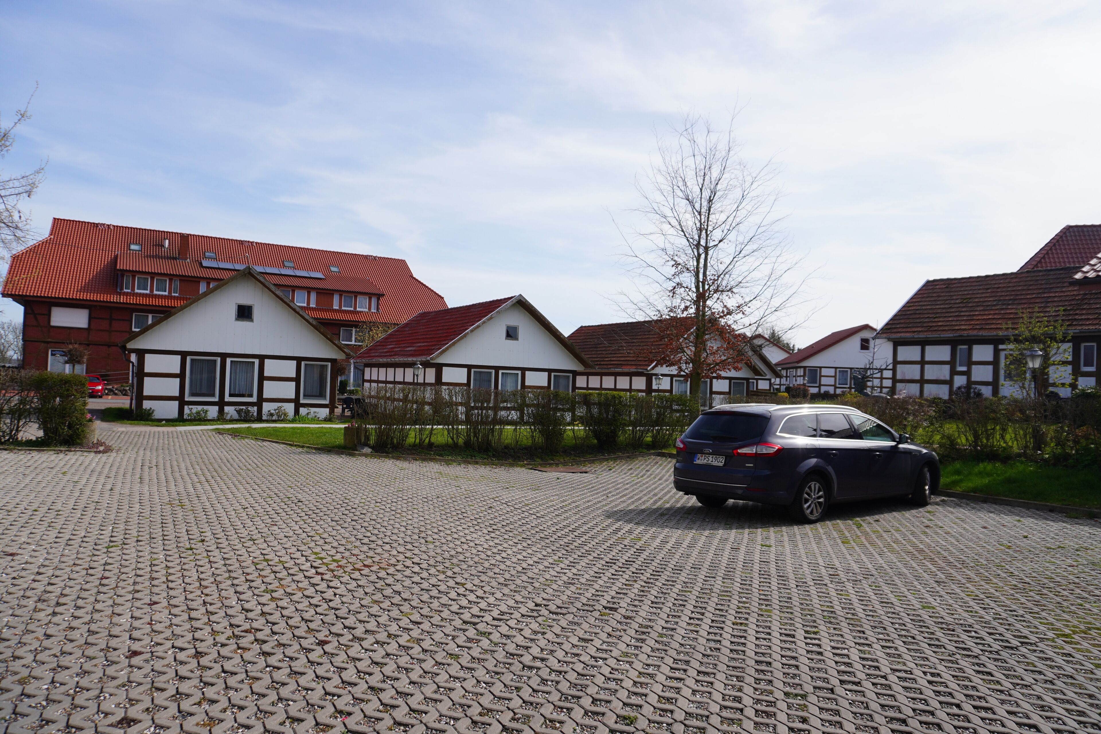 A residential area with a paved driveway, a parked car, and houses with red roofs and white facades.