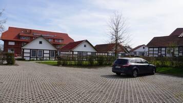A residential area with a paved driveway, a parked car, and houses with red roofs and white facades.