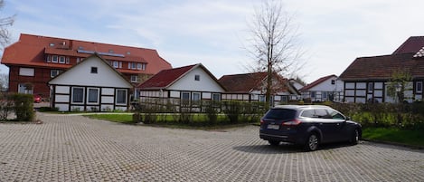 Una zona residencial con un camino pavimentado, un automóvil estacionado y casas con tejados rojos y fachadas blancas.
