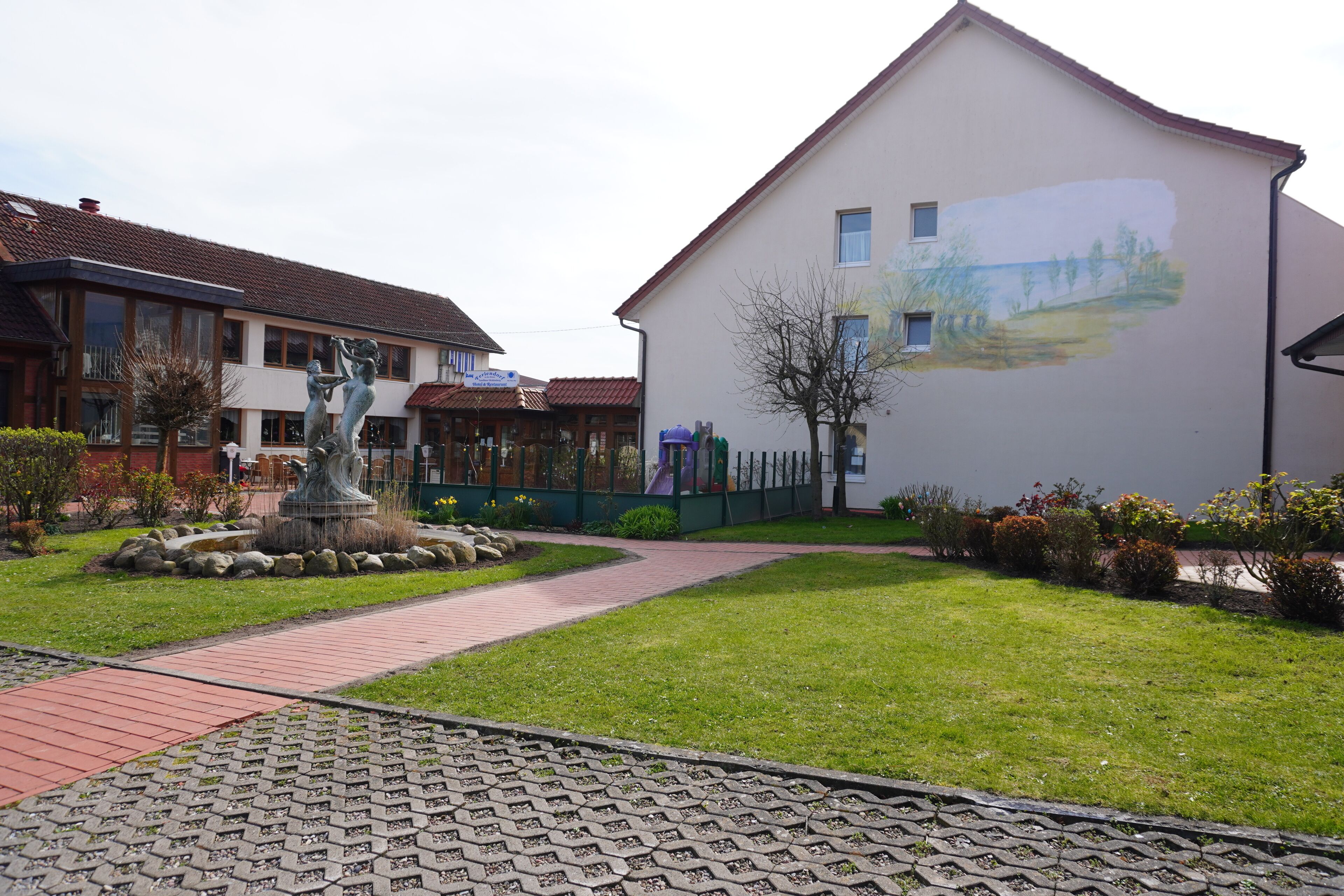 Ein Innenhof mit einer Statue, einem Wandgemälde an einem Gebäude und einem gepflasterten Weg.