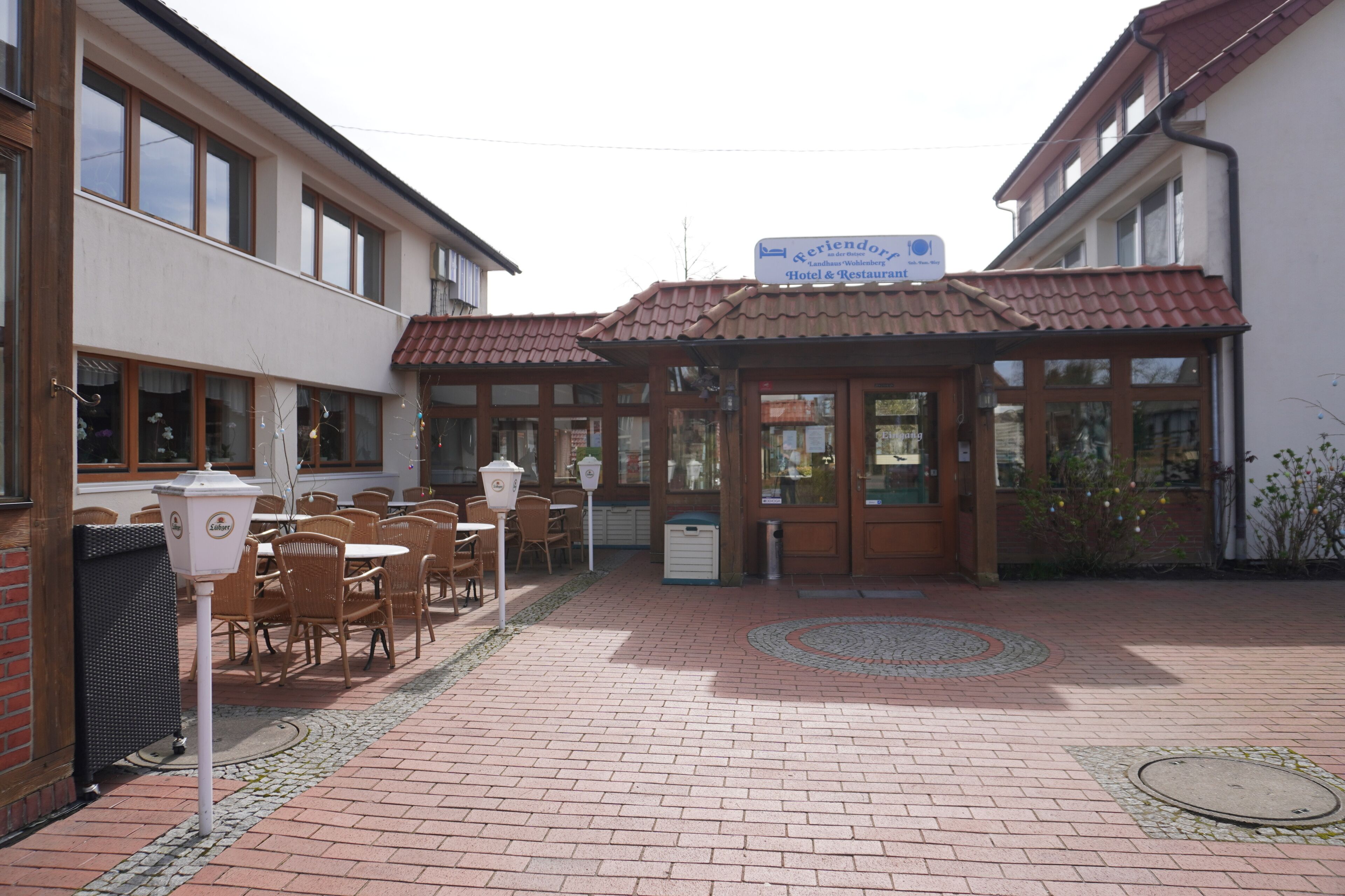 Un patio de hotel con asientos al aire libre, un letrero que indica un restaurante y un suelo de ladrillo con diseño.