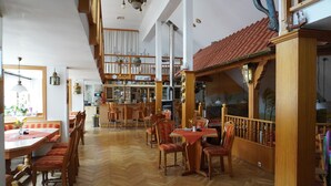 A spacious dining area with wooden tables and chairs, a bar area with shelves of bottles, and a high ceiling with exposed beams.