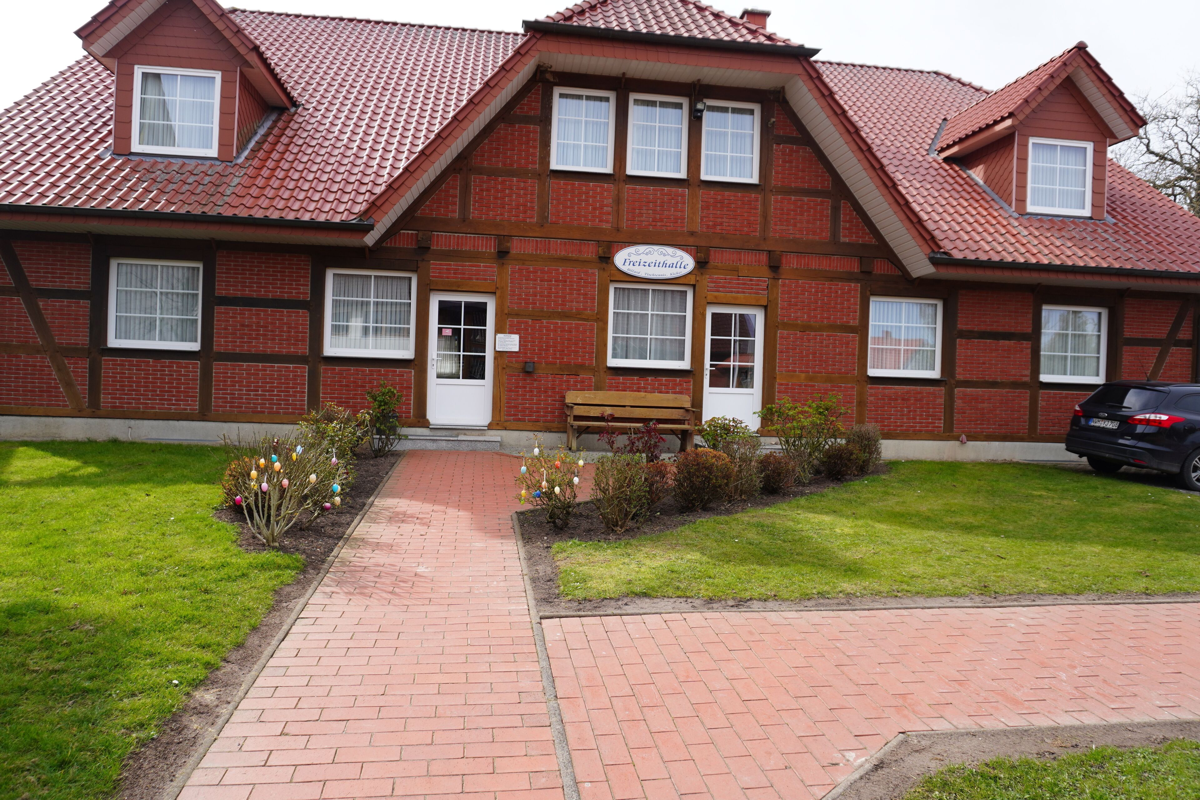 Een traditioneel vakwerkhuis met een rode dakbedekking, een houten bank ervoor en een geplaveid pad dat naar de ingang leidt.