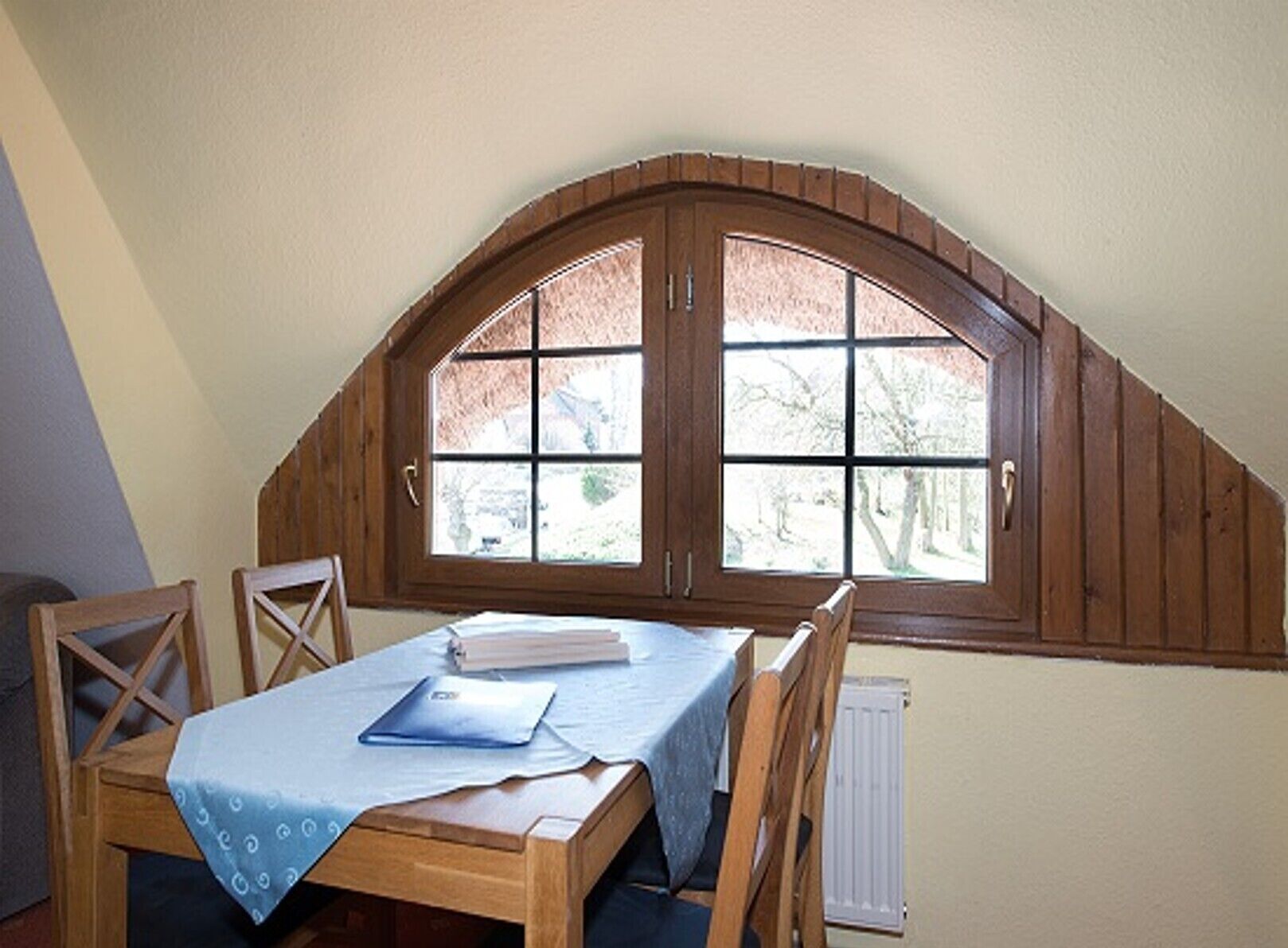 A dining area with a wooden table and chairs, a window with a wooden frame, and a radiator below the window.