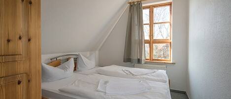 A bedroom with a wooden bed frame, white bedding, a window with curtains, and a wooden door.
