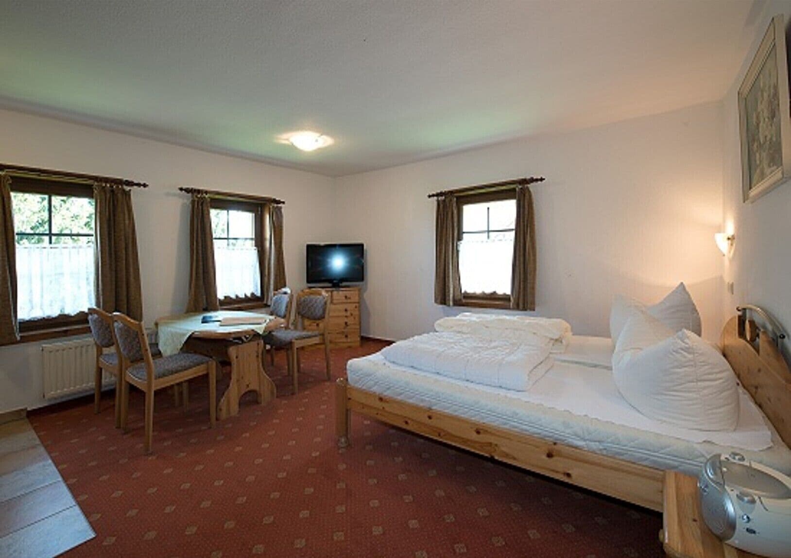 A bedroom with a bed, a desk, a chair, a television, and a radiator.