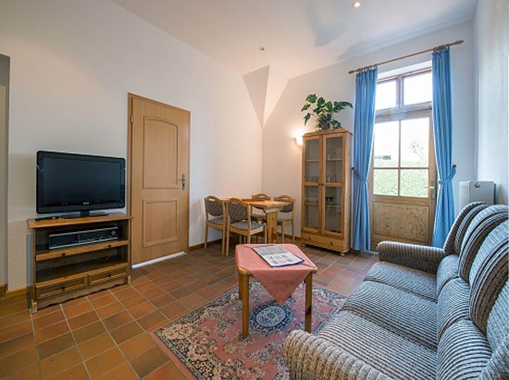 A living room with a television, a dining table with chairs, a sofa, a cabinet, and a window with curtains.