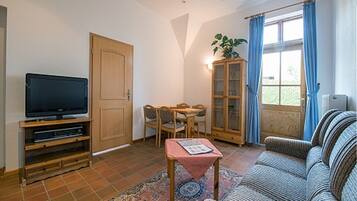 A living room with a television, a dining table with chairs, a sofa, a cabinet, and a window with curtains.