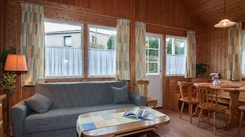 A cozy wooden cabin interior with a sofa, dining table, chairs, and large windows.