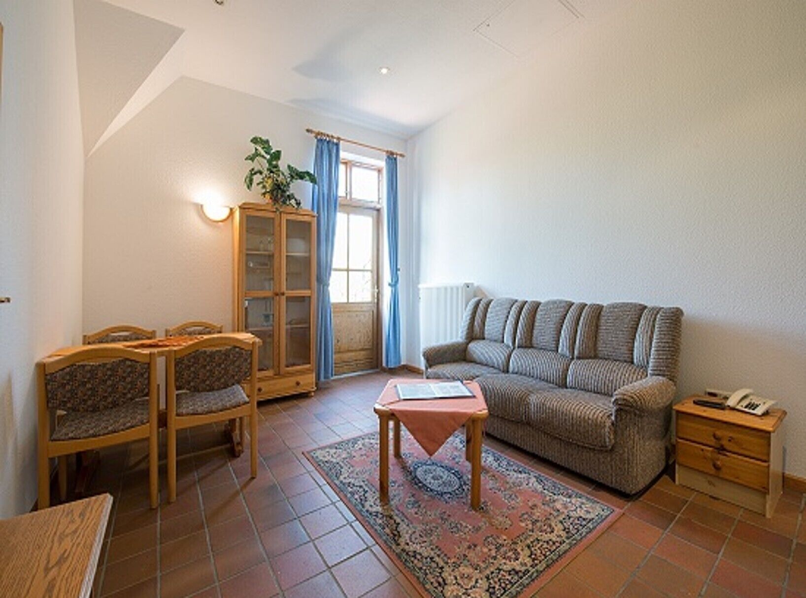 Una sala de estar acogedora con un sofá, dos sillones, una mesita, un aparador y una ventana con cortinas.