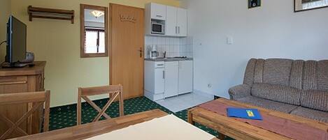 A compact living space with a kitchenette, a sofa, a dining table, and a TV.