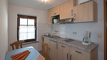 A compact kitchen with wooden cabinets, a microwave, a coffee maker, and a window with a curtain.