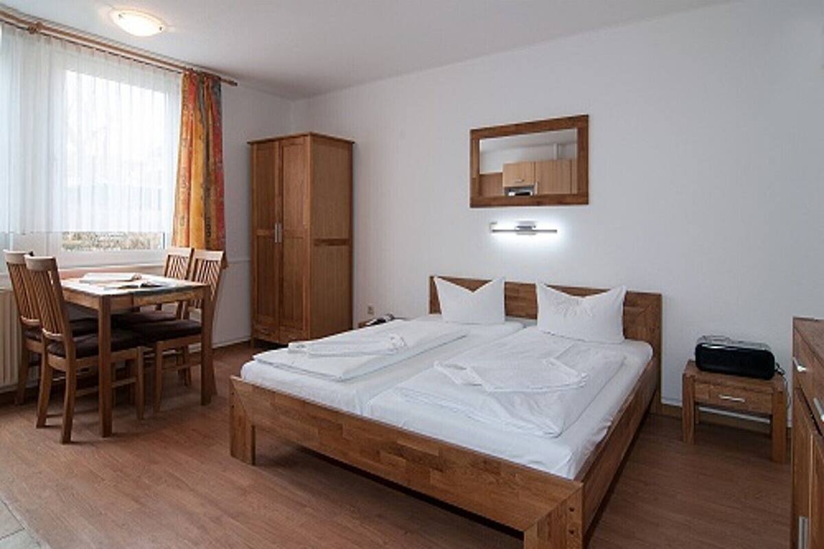 Una habitació amb un llit de fusta, un escriptori amb cadires, un armari i un mirall a la paret.