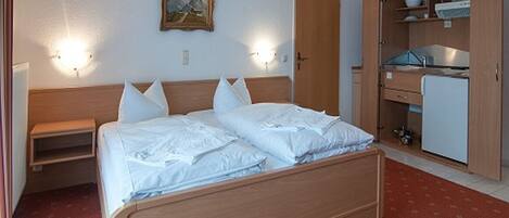 A hotel room with a wooden bed, a nightstand, a wardrobe, and a small desk with a chair.