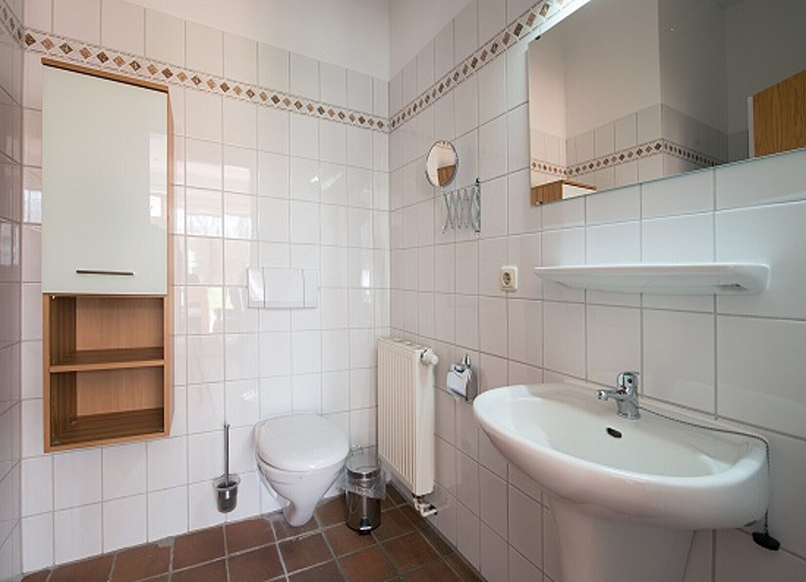 A bathroom with white tiles, a toilet, a sink, a mirror, and a towel rack.