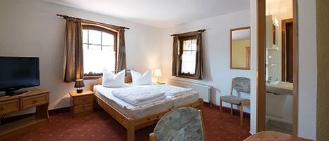 Een hotelkamer met een bed, een bureau, een stoel, een televisie en een badkamer, zichtbaar door een geopende deur.