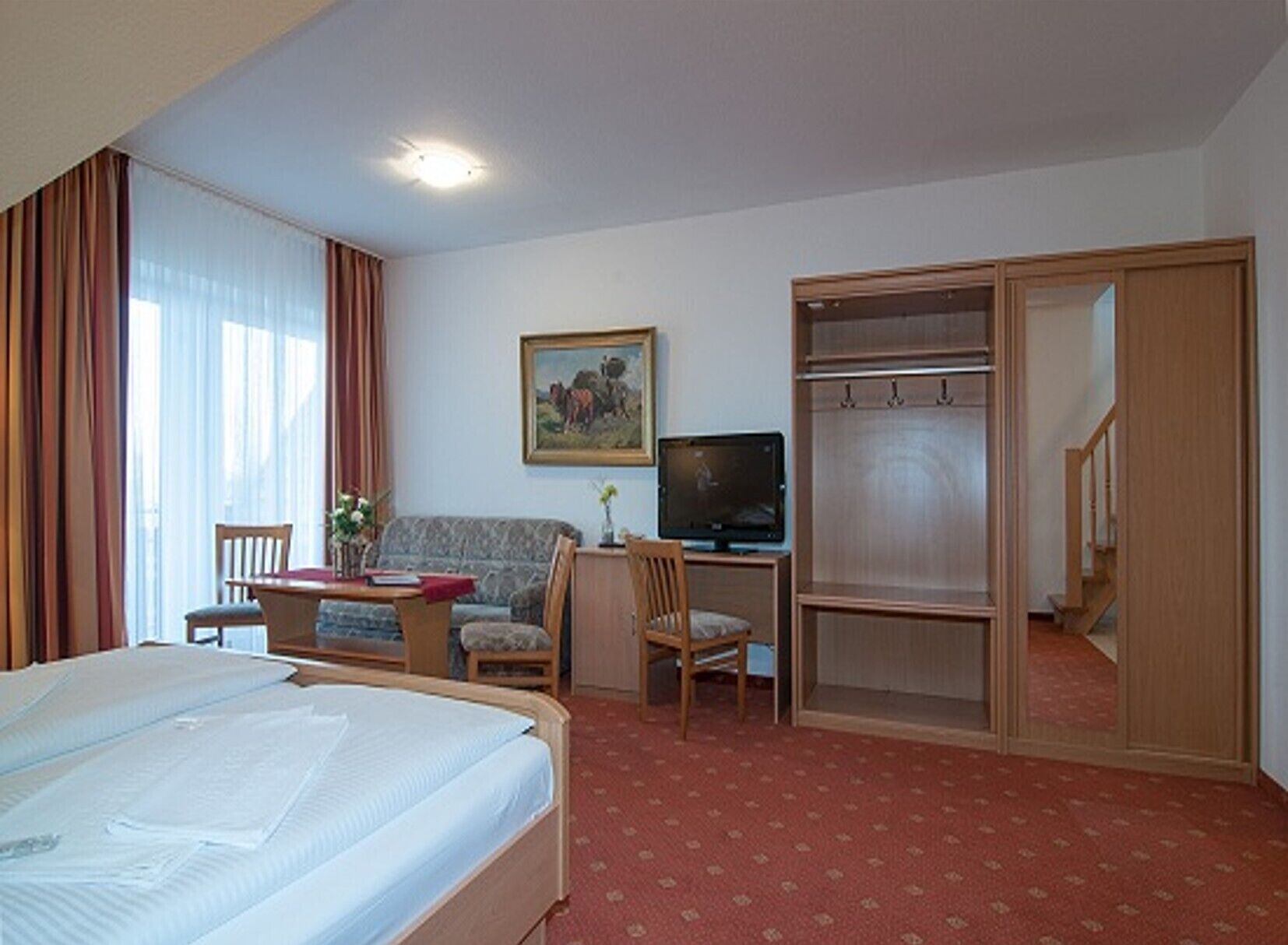Et hotelværelse med en seng, et skrivebord med computer, en stol, en sofa og et klædeskab.